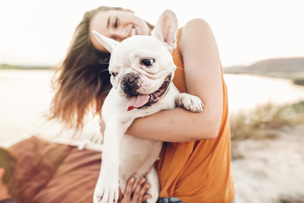 Woman holding french bulldog puppy on the beach.